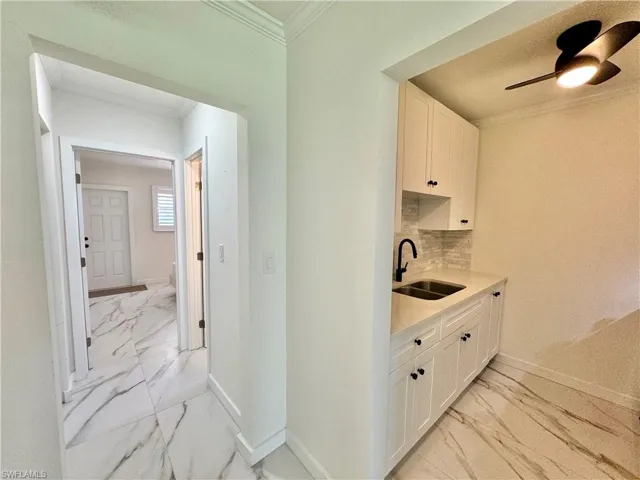 Kitchen featuring ceiling fan, tasteful backsplash, light tile floors, sink, and white cabinetry