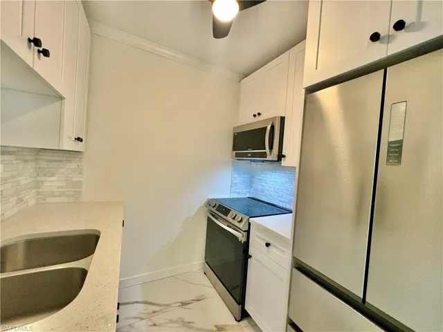 Kitchen featuring appliances with stainless steel finishes, white cabinetry, backsplash, and ceiling fan
