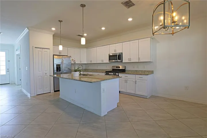 Kitchen with crown molding, white cabinets, dark stone counters, stainless steel appliances, and light tile patterned flooring