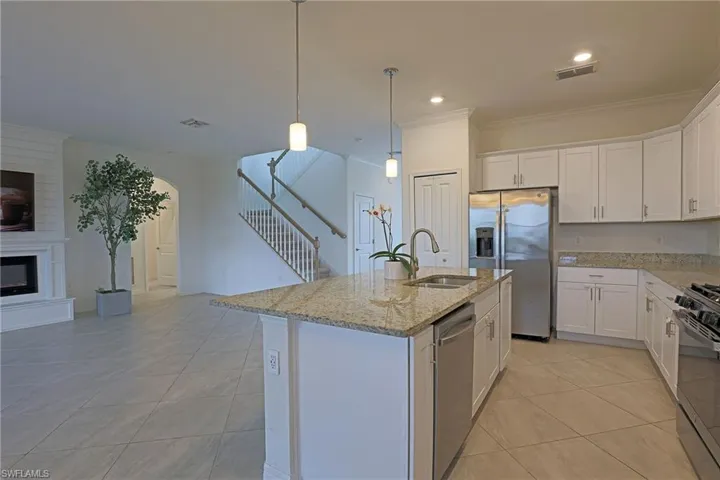 Kitchen featuring white cabinets, stainless steel appliances, light stone countertops, ornamental molding, and decorative light fixtures