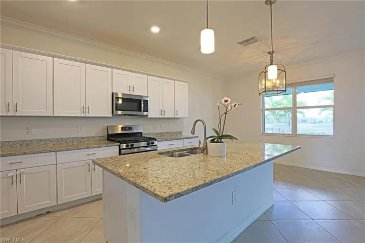 Kitchen featuring stainless steel appliances, white cabinets, light stone counters, light tile patterned floors, and an island with sink