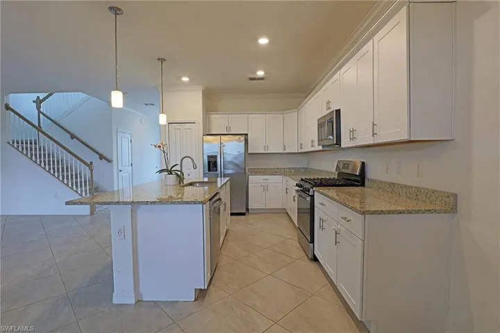 Kitchen featuring stainless steel appliances, white cabinetry, light stone countertops, pendant lighting, and an island with sink