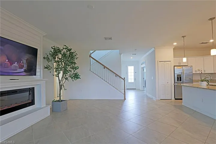 Unfurnished living room with ornamental molding, light tile patterned floors, and a glass covered fireplace