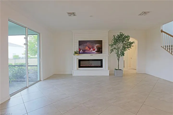 Unfurnished living room featuring light tile patterned flooring, a glass covered fireplace, crown molding, and arched walkways