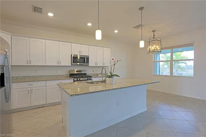 Kitchen with white cabinetry, light stone counters, light tile patterned floors, and crown molding