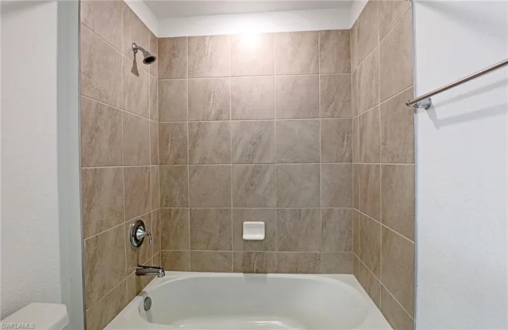Bathroom with tub / shower combination and a textured wall