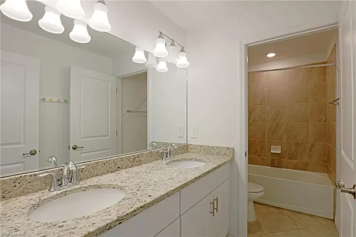 Full bath with double vanity, bathing tub / shower combination, and light tile patterned flooring