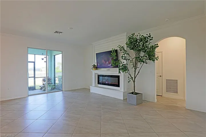 Unfurnished living room featuring arched walkways, light tile patterned floors, crown molding, and a glass covered fireplace