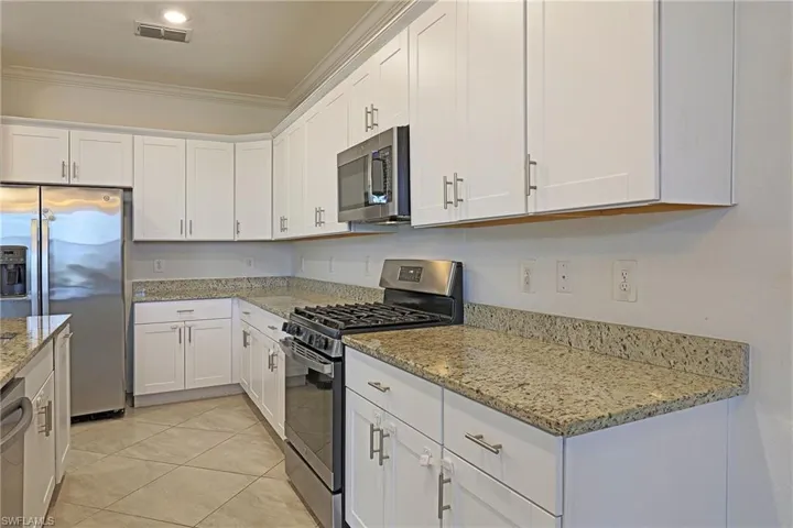 Kitchen with stainless steel appliances, white cabinets, ornamental molding, light stone countertops, and light tile patterned floors