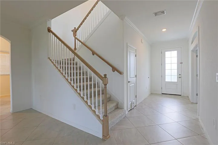 Entrance foyer with arched walkways, ornamental molding, and light tile patterned floors