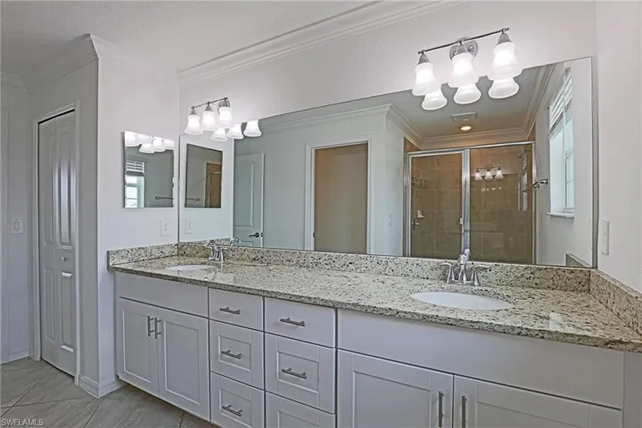 Bathroom featuring a closet, double vanity, a shower stall, and crown molding