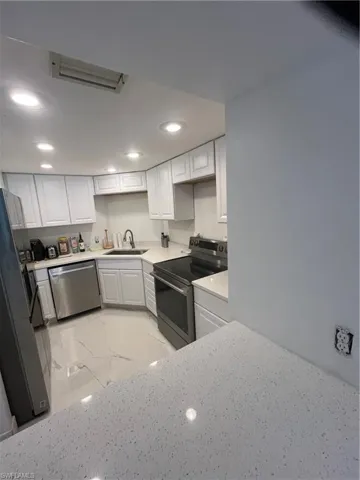 Kitchen with range, white cabinets, light marble finish floors, fridge, and recessed lighting