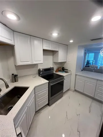 Kitchen featuring stainless steel range, white cabinets, recessed lighting, light stone counters, and light marble finish flooring