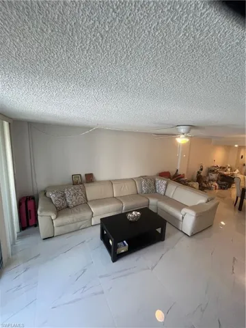 Living room with ceiling fan, a textured ceiling, and light marble finish flooring