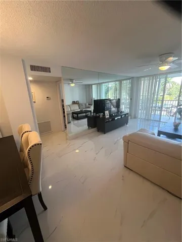 Living room with a ceiling fan, floor to ceiling windows, a textured ceiling, and light marble finish flooring