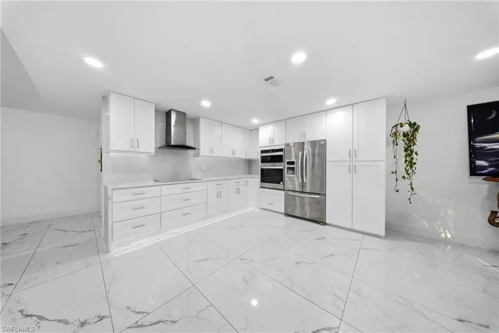 Kitchen with white cabinets, stainless steel appliances, decorative backsplash, light marble finish floors, and recessed lighting