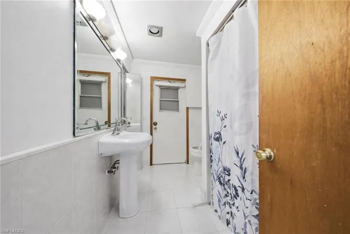 Full bath featuring ornamental molding, a shower with shower curtain, and light tile patterned floors