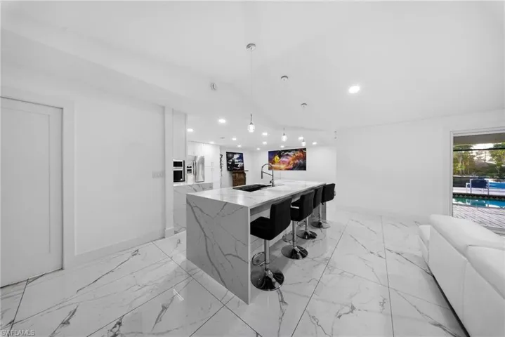 Bar area featuring modern cabinets, white cabinetry, pendant lighting, light stone countertops, and stainless steel refrigerator with ice dispenser