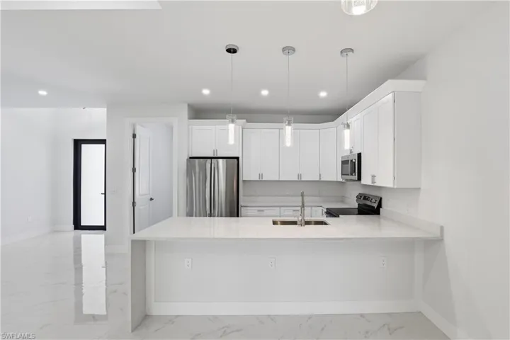 Kitchen featuring a peninsula, stainless steel appliances, light stone countertops, white cabinets, and light marble finish flooring