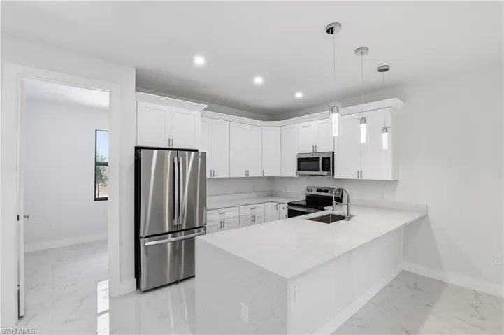 Kitchen with stainless steel appliances, a peninsula, light stone countertops, white cabinets, and light marble finish floors