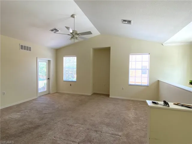 Spare room featuring light colored carpet, vaulted ceiling, and a ceiling fan