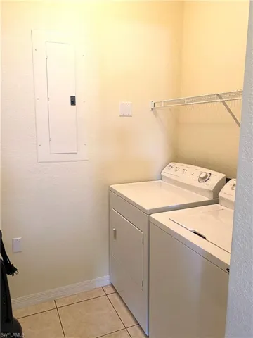 Washroom featuring light tile patterned flooring, electric panel, separate washer and dryer, and a textured wall
