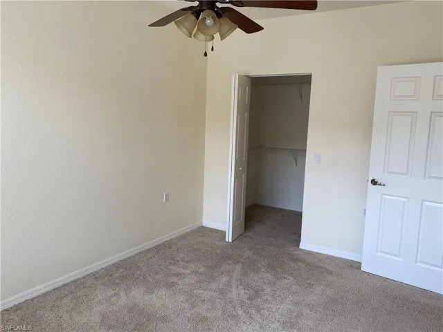 Unfurnished bedroom featuring a walk in closet, carpet floors, and ceiling fan