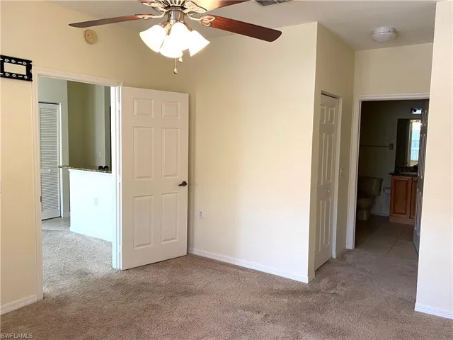 Unfurnished bedroom with connected bathroom, light carpet, a ceiling fan, and a closet
