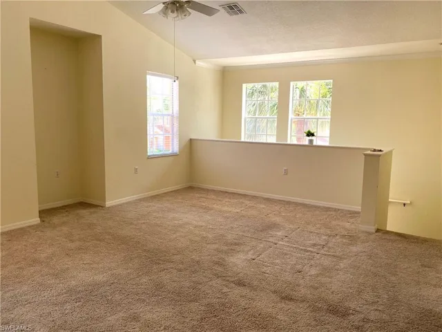 Unfurnished room featuring light carpet, a ceiling fan, vaulted ceiling, and a textured ceiling