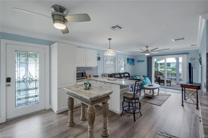 Kitchen with a ceiling fan, a peninsula, light stone counters, white cabinets, and ornamental molding