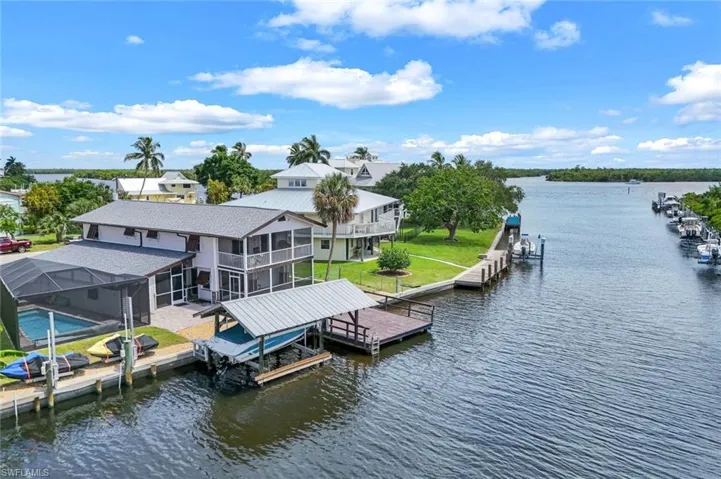 Dock area with boat lift, a water view, a sunroom, and a lawn