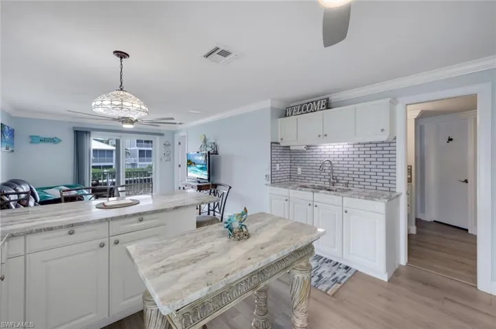 Kitchen with ceiling fan, decorative backsplash, ornamental molding, white cabinets, and decorative light fixtures