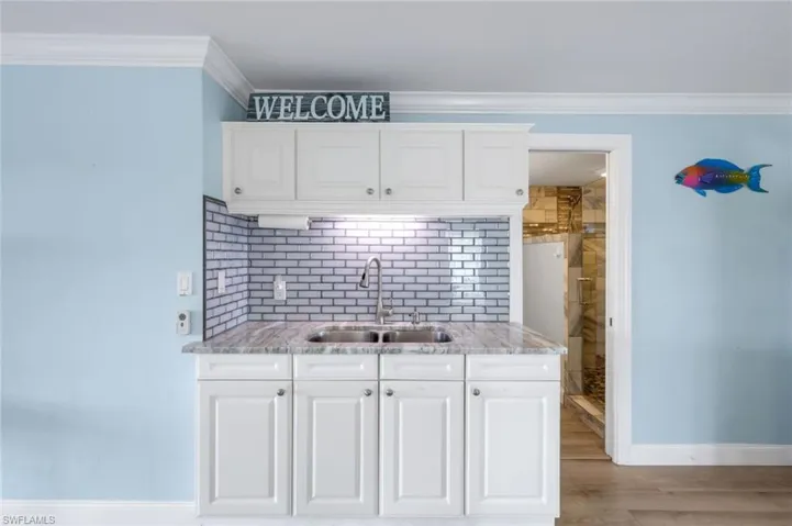 Kitchen with white cabinets, backsplash, crown molding, light stone counters, and light wood-style floors