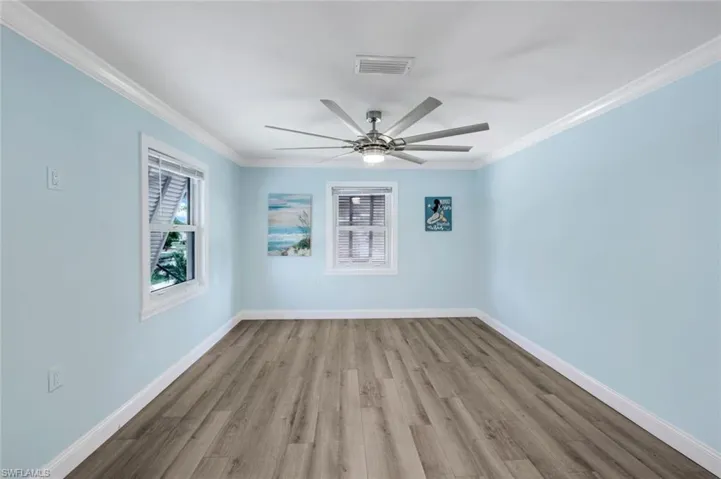 Empty room featuring healthy amount of natural light, wood finished floors, crown molding, and ceiling fan