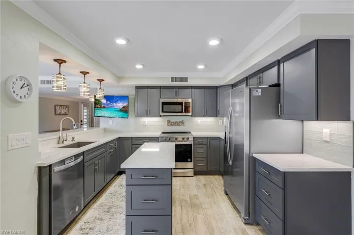Kitchen featuring crown molding, backsplash, light stone countertops, gray cabinetry, and appliances with stainless steel finishes