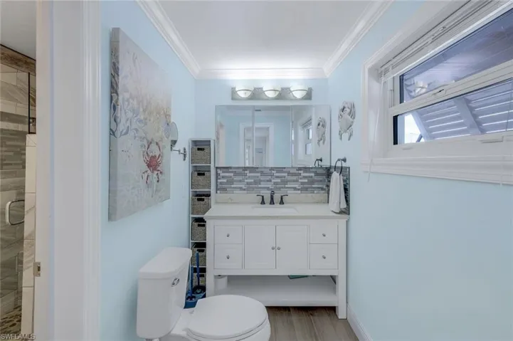 Full bathroom featuring tasteful backsplash, a stall shower, vanity, ornamental molding, and light wood-style floors