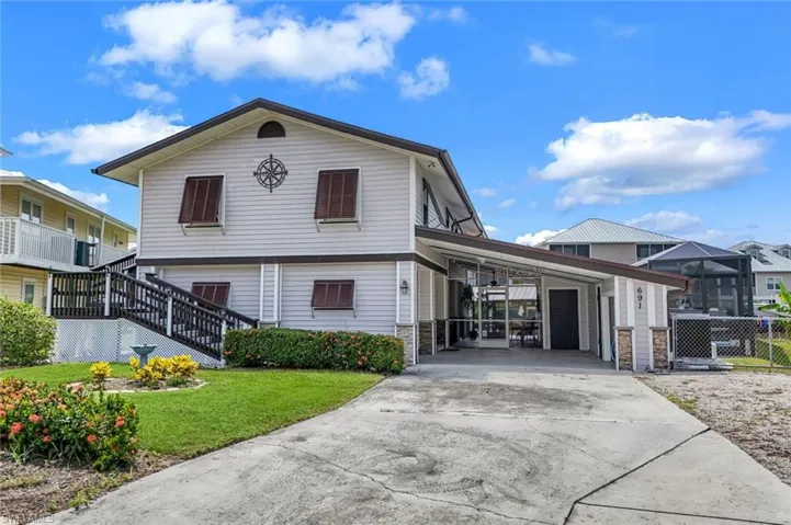 View of front of house featuring driveway, stone siding, stairway, and an attached carport