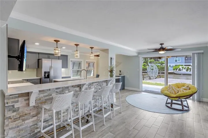 Kitchen featuring gray cabinetry, a kitchen bar, stainless steel fridge with ice dispenser, light wood-style floors, and crown molding