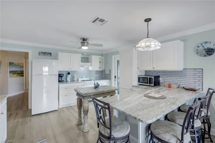 Kitchen with backsplash, a peninsula, white appliances, a breakfast bar area, and ornamental molding
