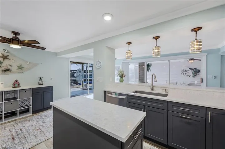 Kitchen with ceiling fan, a center island, pendant lighting, dishwasher, and light stone counters