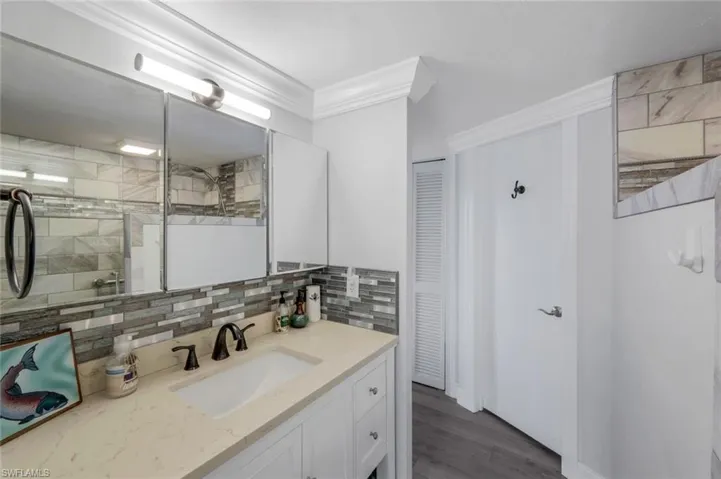 Full bathroom with vanity, a closet, crown molding, decorative backsplash, and dark wood-style floors