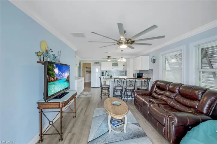 Living room featuring ornamental molding, light wood-type flooring, and a ceiling fan