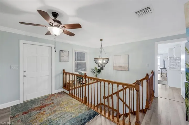 Stairs with crown molding, wood finished floors, a ceiling fan, and a chandelier