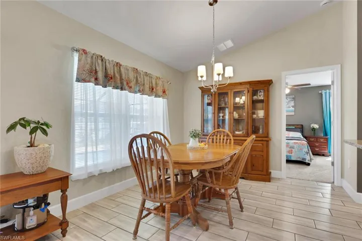 Vaulted ceiling dining area featuring tile flooring, a window with blinds, and a multi-light chandelier