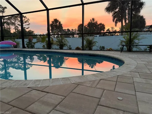 Screened pool enclosure featuring a curved-edge pool with tiled coping, surrounded by a paver patio