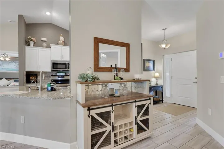 Bright entryway featuring a white paneled door with sidelight, tile flooring, and a decorative serving cabinet with wine storage