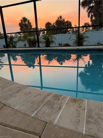 Swimming pool featuring brick-patterned coping, screened enclosure, and tropical landscaping with mature palm trees