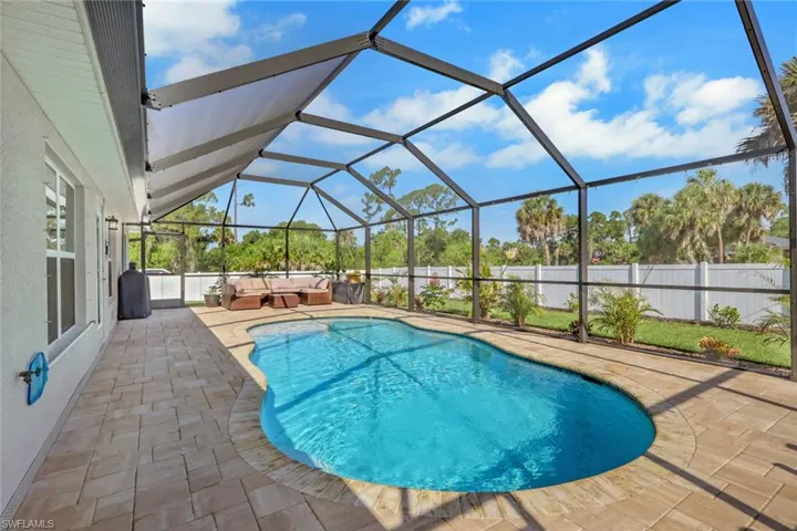 Screened-in outdoor living space featuring a freeform swimming pool, paver deck, and white privacy fencing