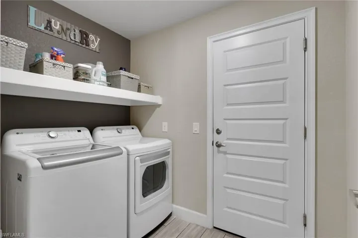 Dedicated laundry area featuring a white paneled door, floating wall shelves, contrasting two-tone wall finishes, and wood-finish flooring