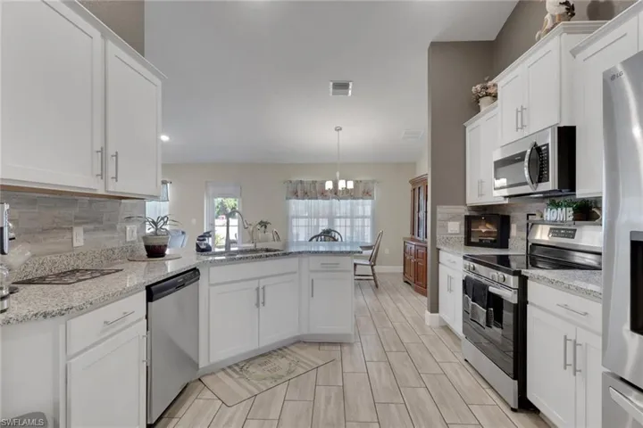 Modern kitchen featuring white cabinetry, granite countertops, stainless steel appliances, a tile backsplash, and wood-finish flooring